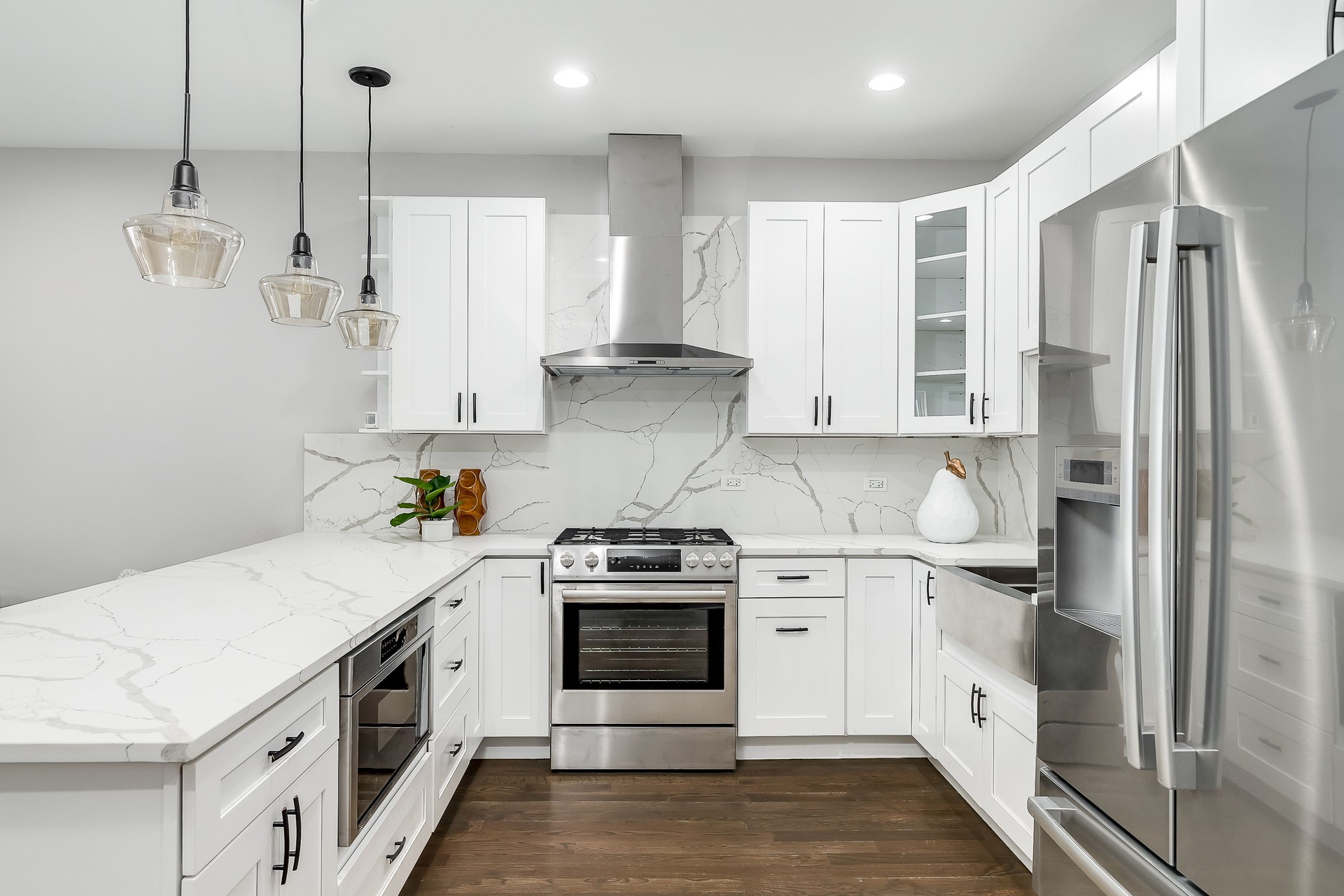 A white kitchen with marble countertops and stainless steel appliances.